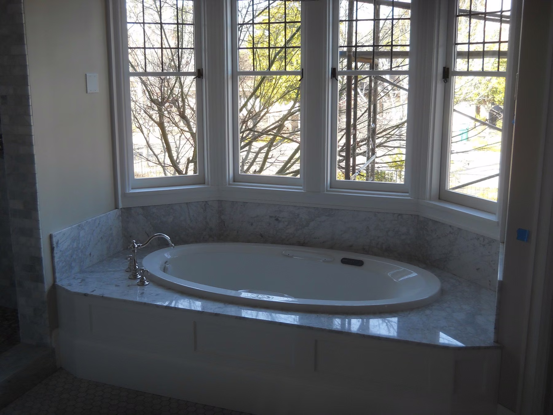 Oval drop-in tub set into a marble deck beneath a bay of leaded-glass windows