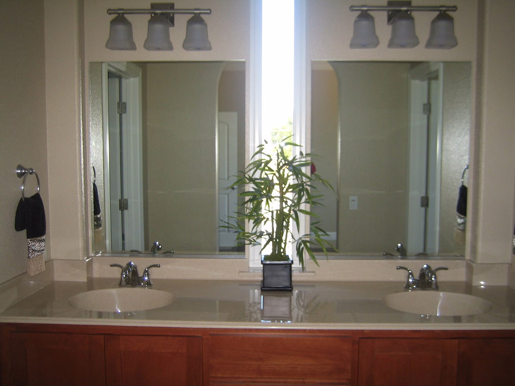 Double vanity with a cherry base, twin mirrors and a window between them carrying a potted plant