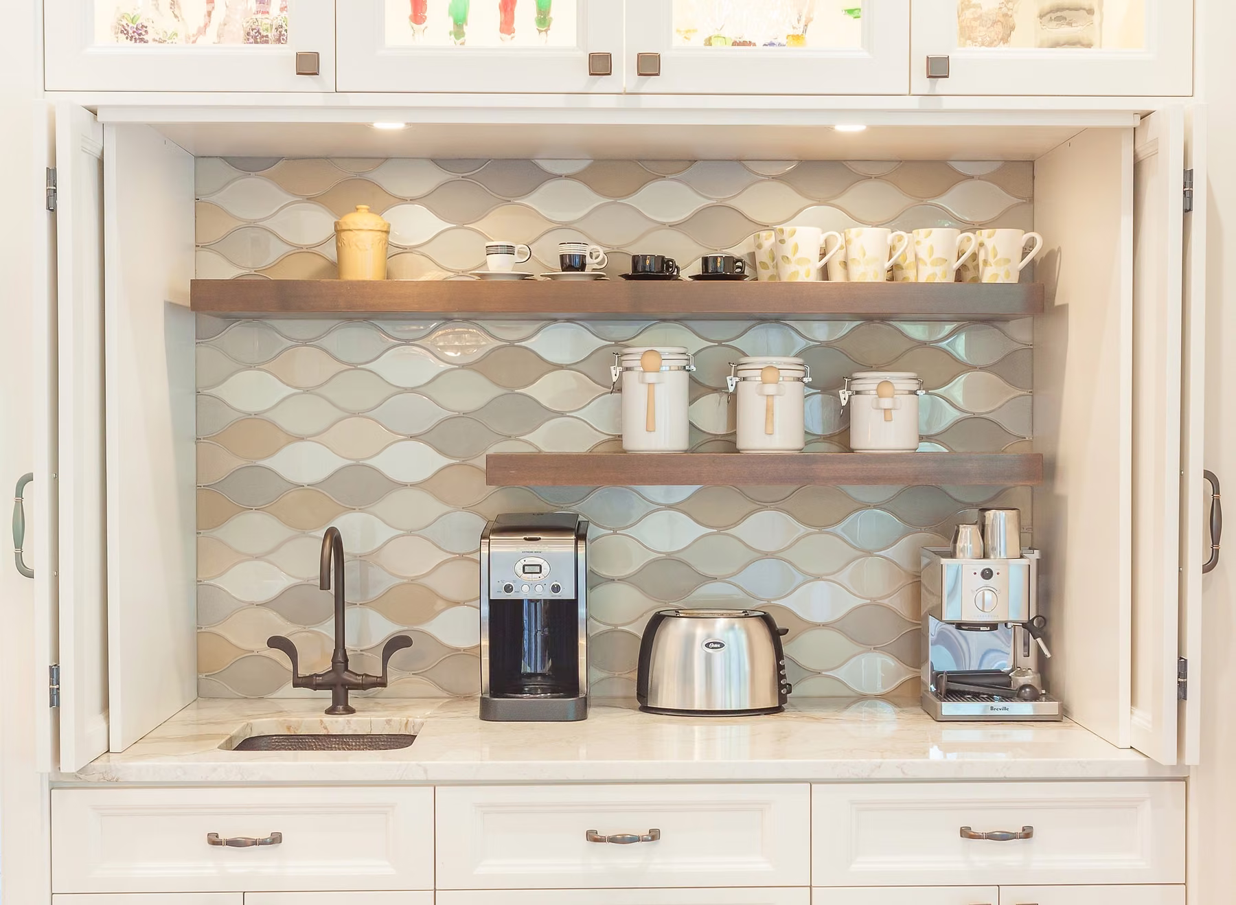 Appliance garage with bi-fold doors open over a prep sink, lit shelves and a scalloped glass tile backsplash