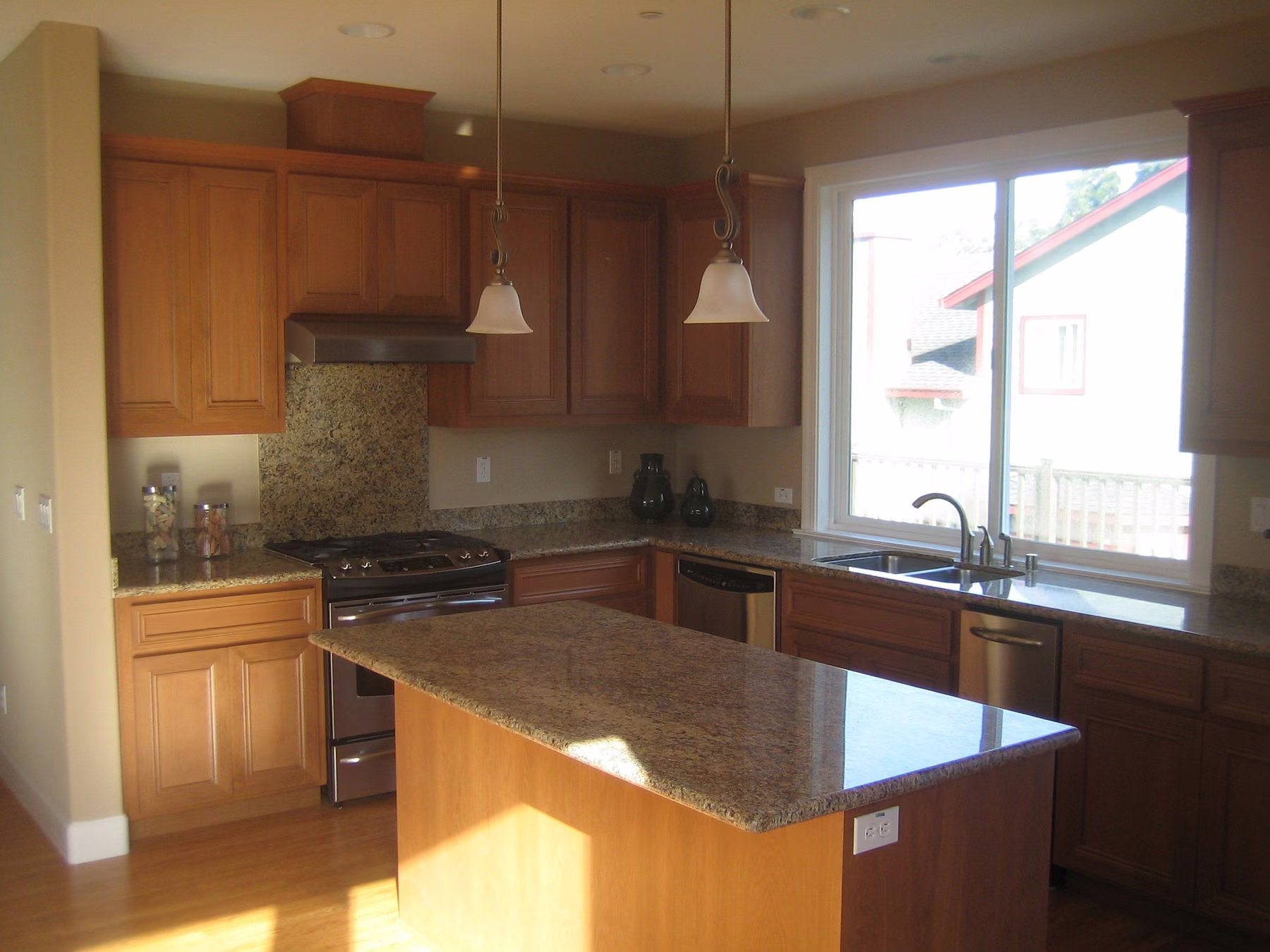 Kitchen with cherry cabinetry, a granite island, pendant lighting and a wide sliding window over the sink