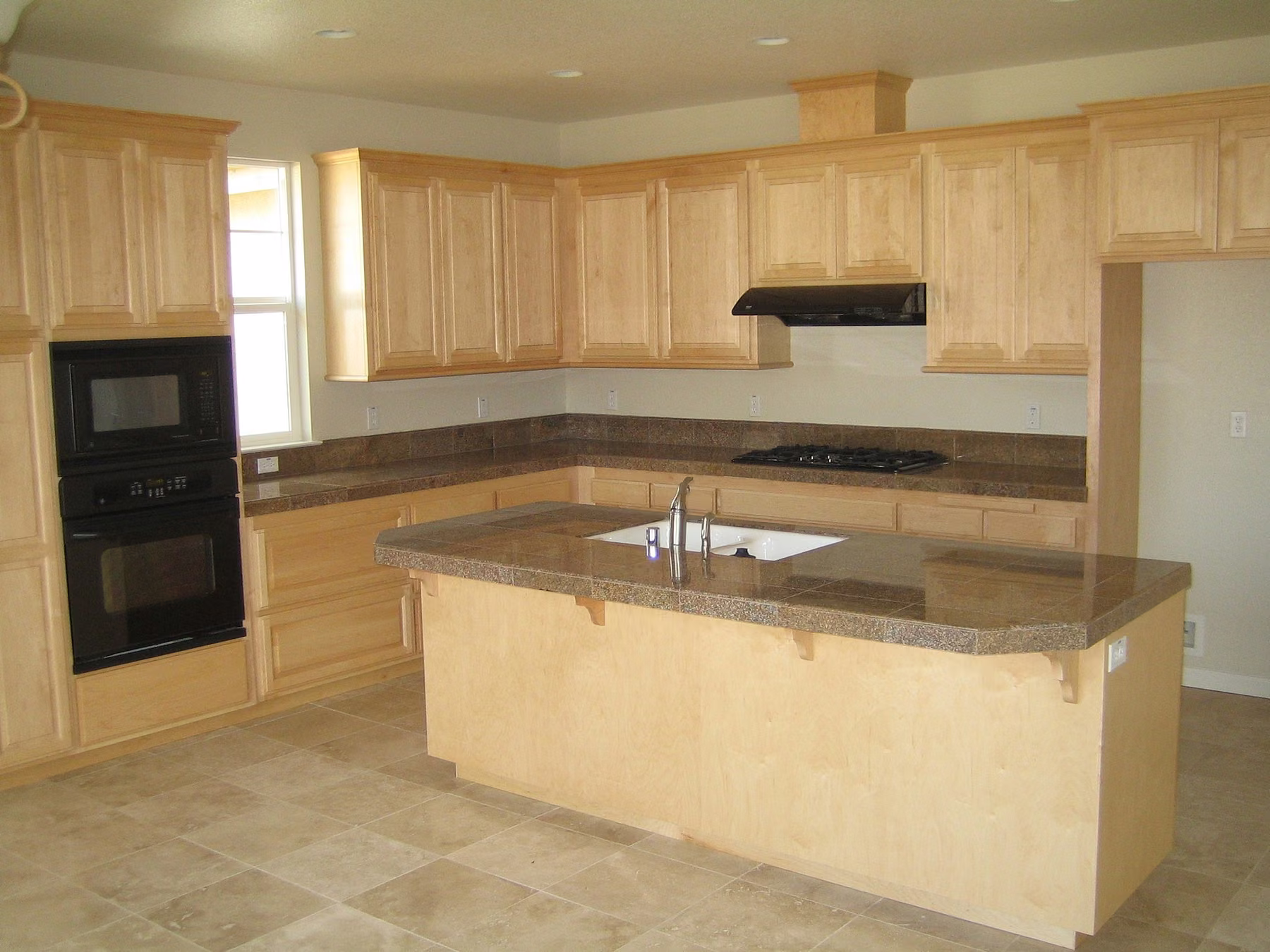 Maple kitchen with a long granite island, black wall ovens and a cooktop set into the island