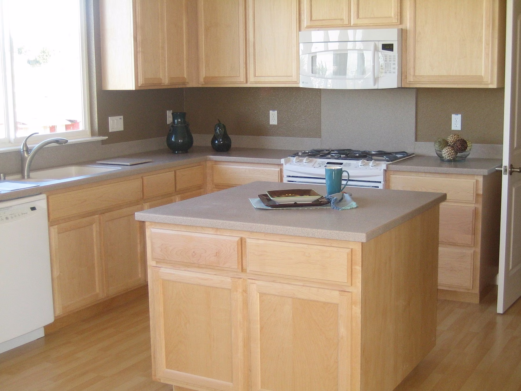 Maple kitchen with a square island, a gas range and a window over the corner sink