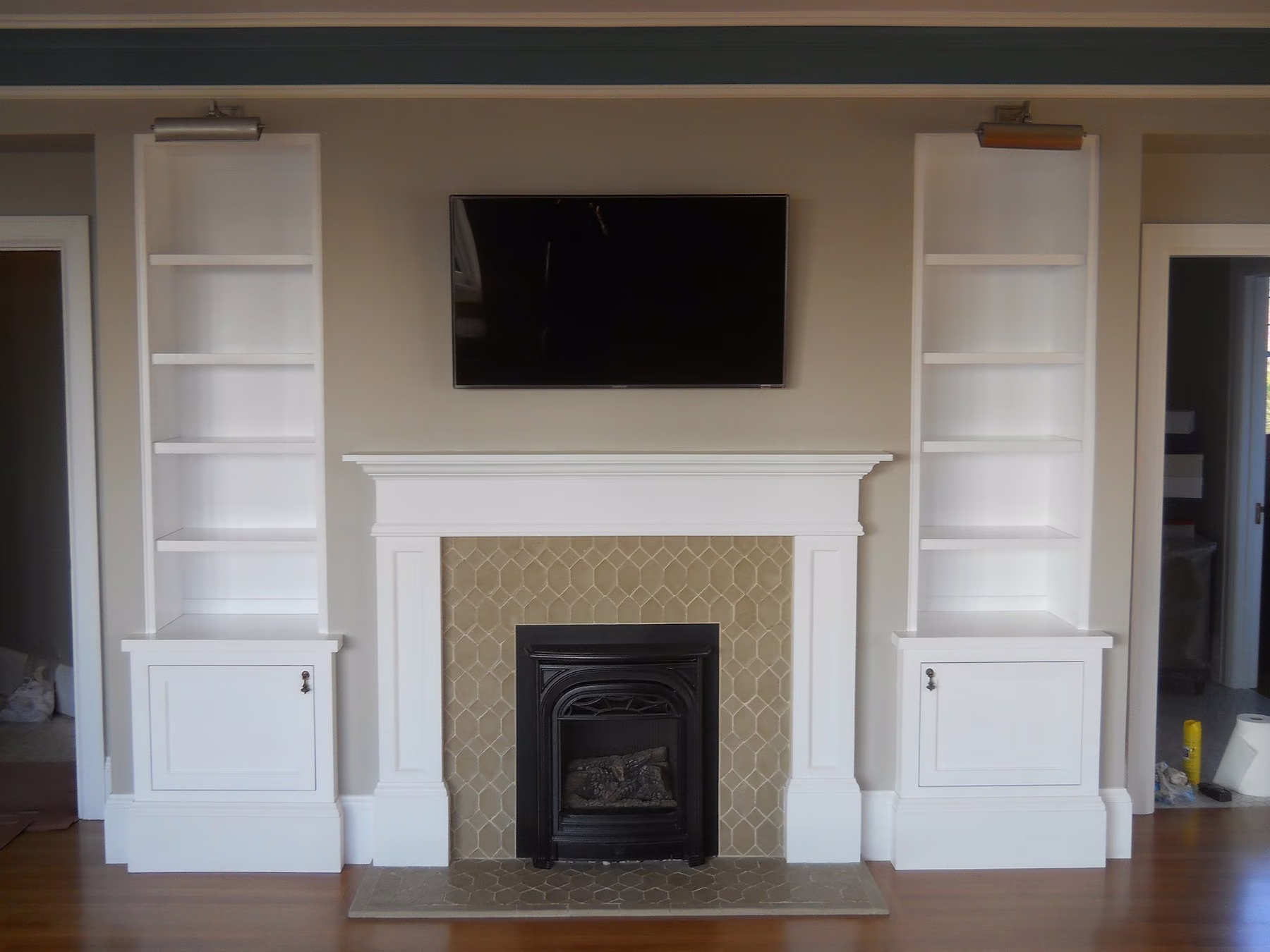 Rebuilt fireplace wall with a painted mantel, patterned tile surround, flanking bookcases and a wall-mounted television