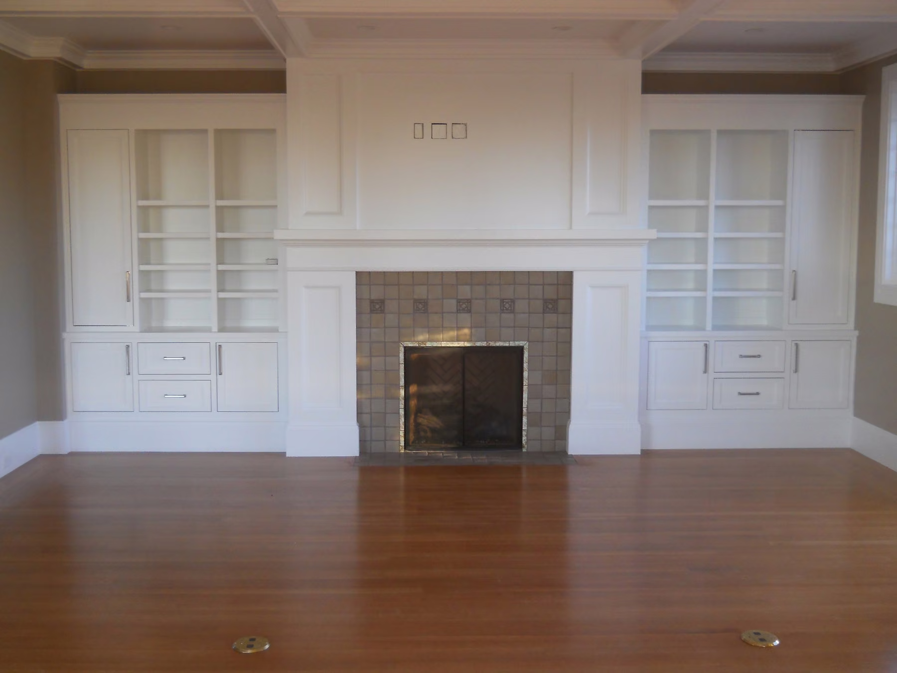 Living room with a tiled fireplace framed by full-height painted bookcases and cabinets, on a refinished hardwood floor